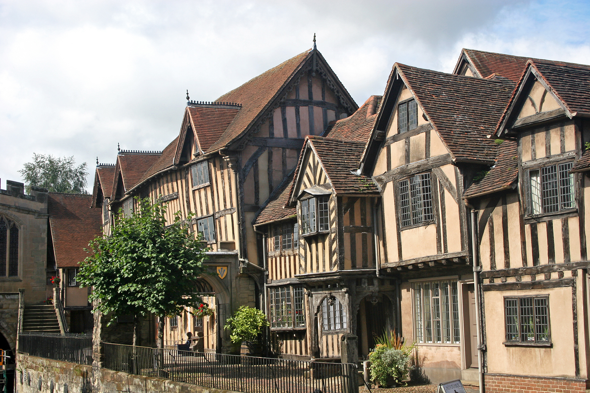 Un ancient édifice de style Tudor avec des poutres de support en bois et un arbre vert devant.